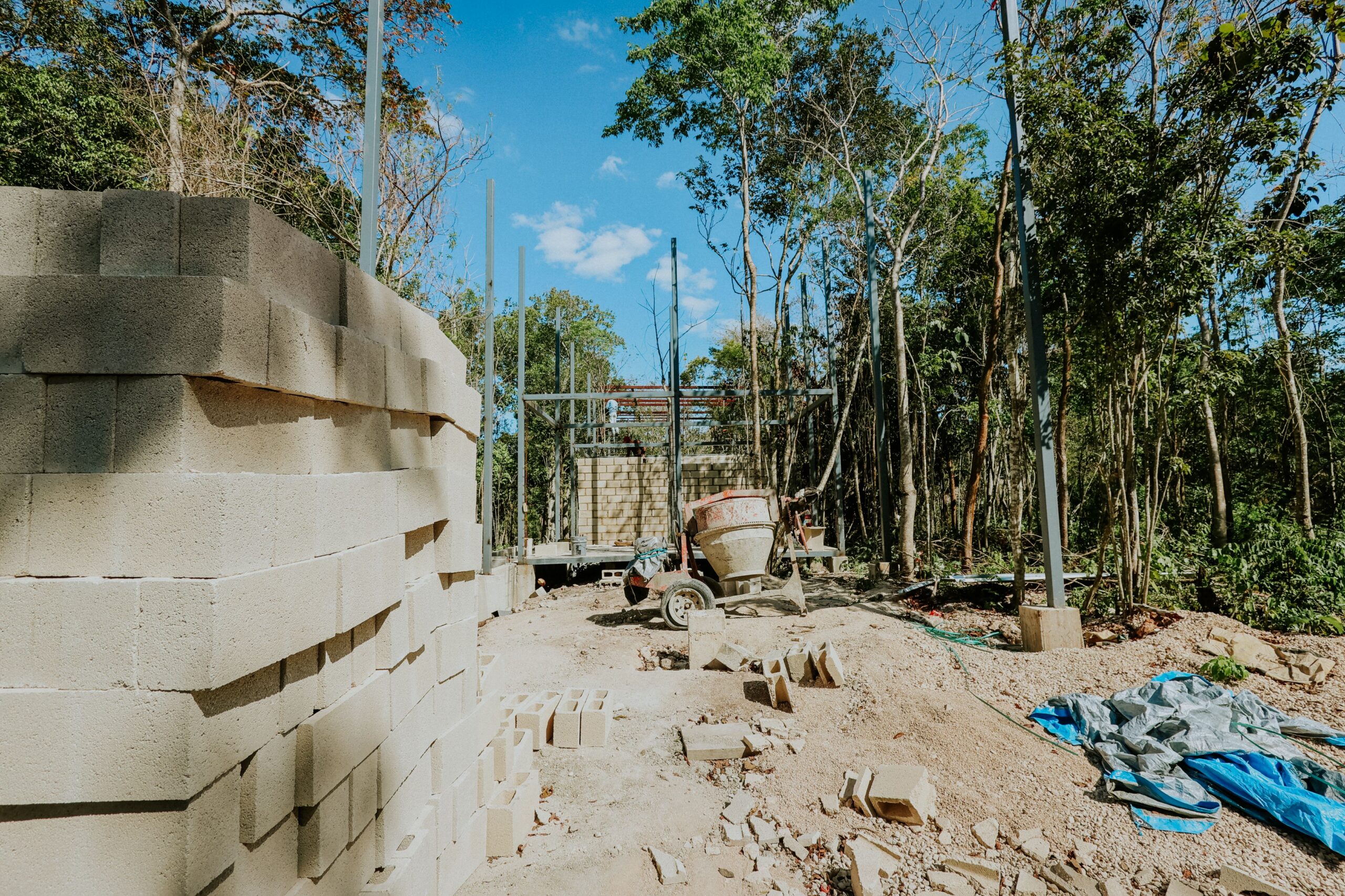 Stacked blocks, cement mixer, and bare soil among trees at a build site needing tree protection in Chattanooga, TN
